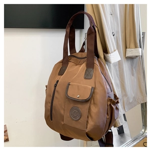 Close-up of coffee brown nylon backpack featuring a leather logo and pleated side pockets
