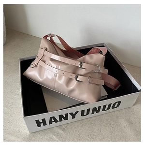 Detail of glossy pink patent leather bag with metal buckle straps and nylon shoulder strap