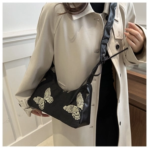 Close-up of golden butterfly embroidery on black textured fabric underarm bag