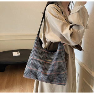 Classic checkered tote bag worn over shoulder featuring black leather strap and brand label