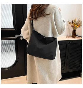 Close-up of black matte tote bag with silver metal snap button and wide shoulder strap
