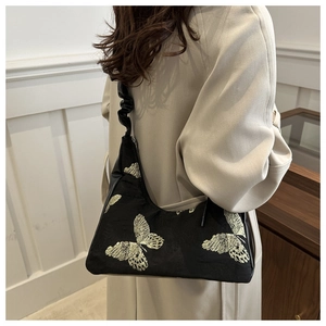 Detail of golden butterfly embroidery on black fabric underarm bag with pleated strap