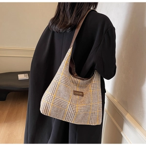 Detail of checkered tote bag with brown leather shoulder strap on model in black coat