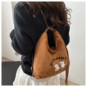 Detailed view of brown suede bucket bag with white puppy embroidery and shoulder strap