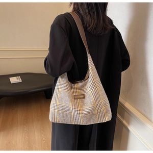 Detail of a large plaid tote bag with brown leather straps shown on model shoulder