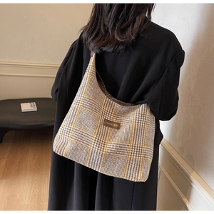 Detail view of large plaid tote bag with brown leather label on textured fabric