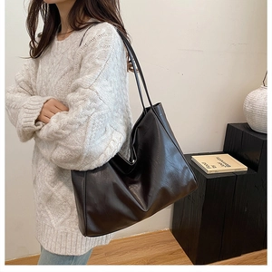 Detail of a black leather tote bag worn over the shoulder by a model in a white sweater