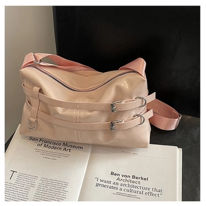Detail of pink pleated leather shoulder bag with decorative straps on a book background