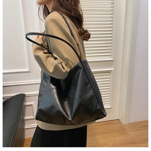 Side view of a black large-capacity tote bag worn by a model in a minimalist indoor setting