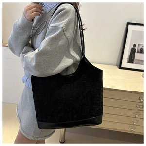 Detail view of large black corduroy tote bag with leather base on model's shoulder