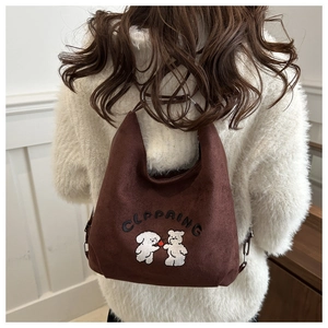 Detail of dark brown faux suede tote bag with cartoon dog embroidery on white sweater