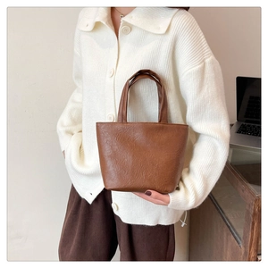 Detail view of the pleated leather texture on a brown square tote bag in a work setting