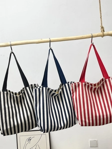 Detailed view of three striped canvas tote bags hanging on a rustic wooden bar