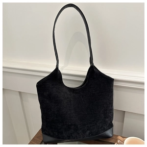 Close-up of black corduroy tote bag with leather straps on minimalist wooden background