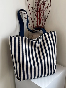 Vertical blue and white striped canvas tote bag displayed on minimalist white stand