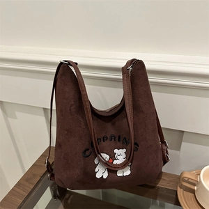 Brown suede tote bag with cute bear embroidery and leather straps on a wooden table