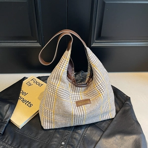 Plaid tote bag with brown leather strap over a vintage black jacket and book background