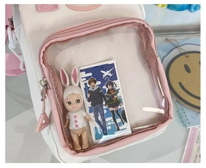 Detail of clear PVC window on pink and white cross-body bag showing doll and cards