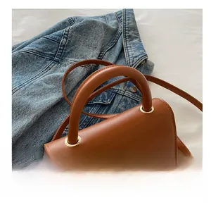 Detailed view of brown leather handbag featuring rounded handle on blue denim jacket