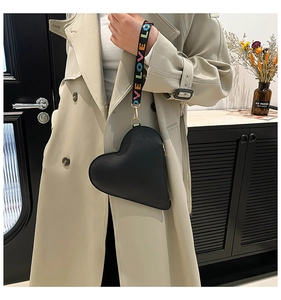 Detail of heart-shaped black leather bag with letter embroidered strap held by a model