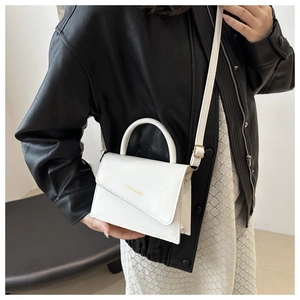 Close-up of stylish white leather handbag with unique asymmetric flap and gold lettering