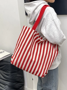 Detailed shot of red and white striped canvas tote bag with red woven straps on a model