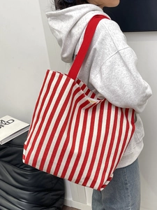 Detailed side view of the striped canvas tote bag worn by a model in casual grey hoodie