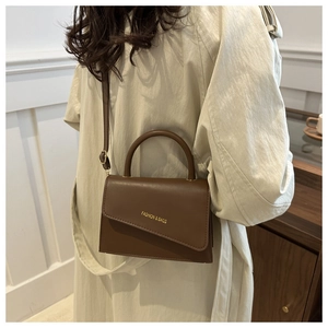 Detailed side view of a brown leather crossbody bag with an asymmetrical flap and golden text