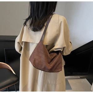 Dettaglio di una borsa hobo in camoscio marrone indossata da una modella in trench beige