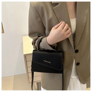 Model wearing a black small cross-body bag with golden text and a top handle
