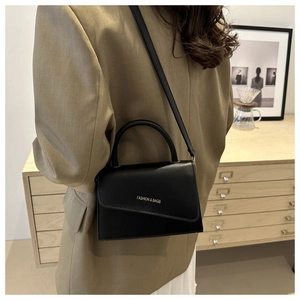 Detailed view of black minimalist handbag with asymmetric flap and fashion lettering