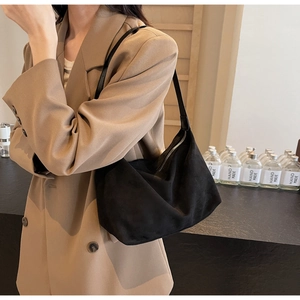 Dettaglio borsa hobo in camoscio nero indossata con un blazer beige per uno stile moderno