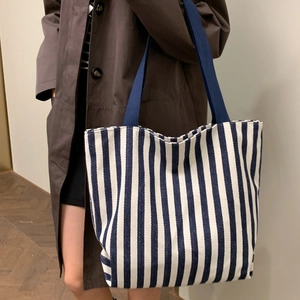 Large blue striped canvas tote bag carried by model in a brown coat for casual daily use