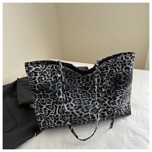 Close-up of a large leopard print tote bag placed on white bedding with a black blazer