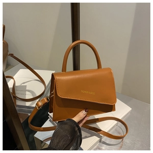 Detail view of brown crossbody bag with asymmetric flap on white books and mirror base