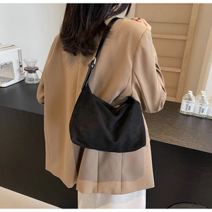 Borsa hobo scamosciata nera sulla spalla di una modella in tailleur color cammello
