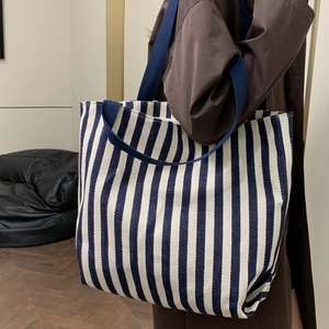 Large blue and white striped canvas tote bag shown as a stylish shoulder bag for women