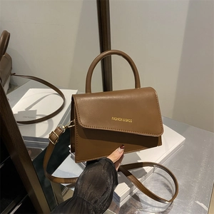 Brown trapezoid handbag with top handle and adjustable strap in a lifestyle setting