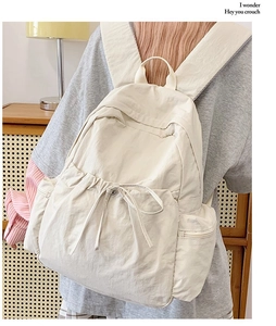 Detail view of cream white nylon backpack featuring drawstring pockets and side zipper closure