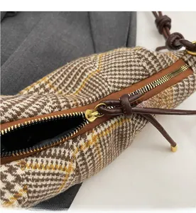 Detailed close-up of smooth metal zipper and brown leather pull on houndstooth fabric bag