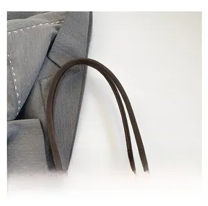 Detailed close-up of smooth brown leather tote handles with fine stitching on grey blazer