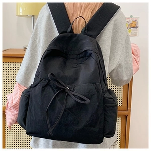 Detail showing the black backpack with a decorative bow and zipper side pockets on a model