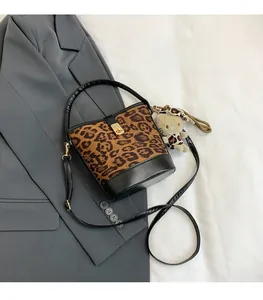 Detail of leopard print bucket bag with golden metal lock and black leather base trim