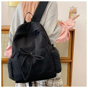 Detail of minimalist black backpack featuring bow decoration and wide ergonomic straps