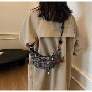 Detail view of plaid crescent bag with cute dog charm on beige coat background