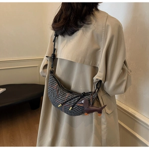 Detail of houndstooth crescent bag with leather dog charm worn over a beige trench coat