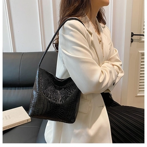 Detail of glossy black crocodile embossed shoulder bag worn by model in a chic interior
