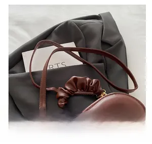 Detail of dark brown heart-shaped bag with pleated handle and golden hardware