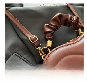 Detail of adjustable gold buckle and pleated handle on dark brown leather heart bag