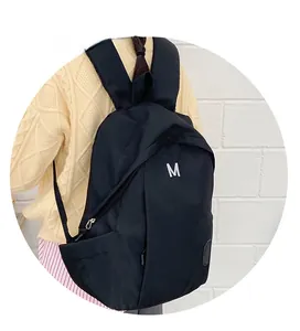 Detailed view of back of a black backpack with padded straps and white letter M embroidery